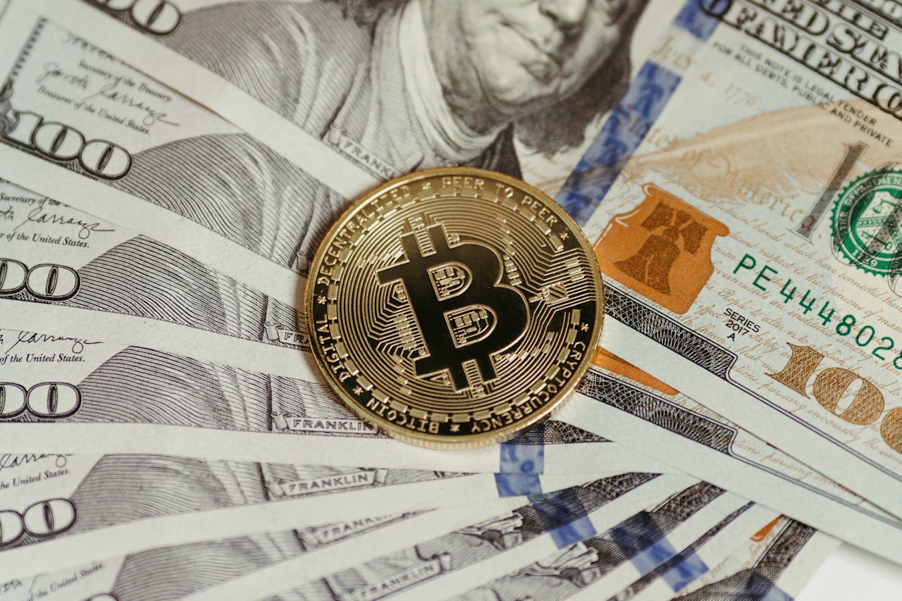 A Bitcoin coin placed on a stack of hundred dollar bills, symbolizing cryptocurrency and traditional wealth.